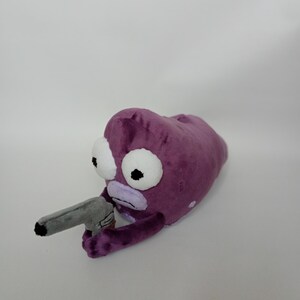Puede incluir: Peluche con forma de alien&iacute;gena morado con grandes ojos blancos y una pistola de juguete gris. El peluche tiene una textura suave y aterciopelada y un dise&ntilde;o de dibujos animados, perfecto para los fans de la serie animada.