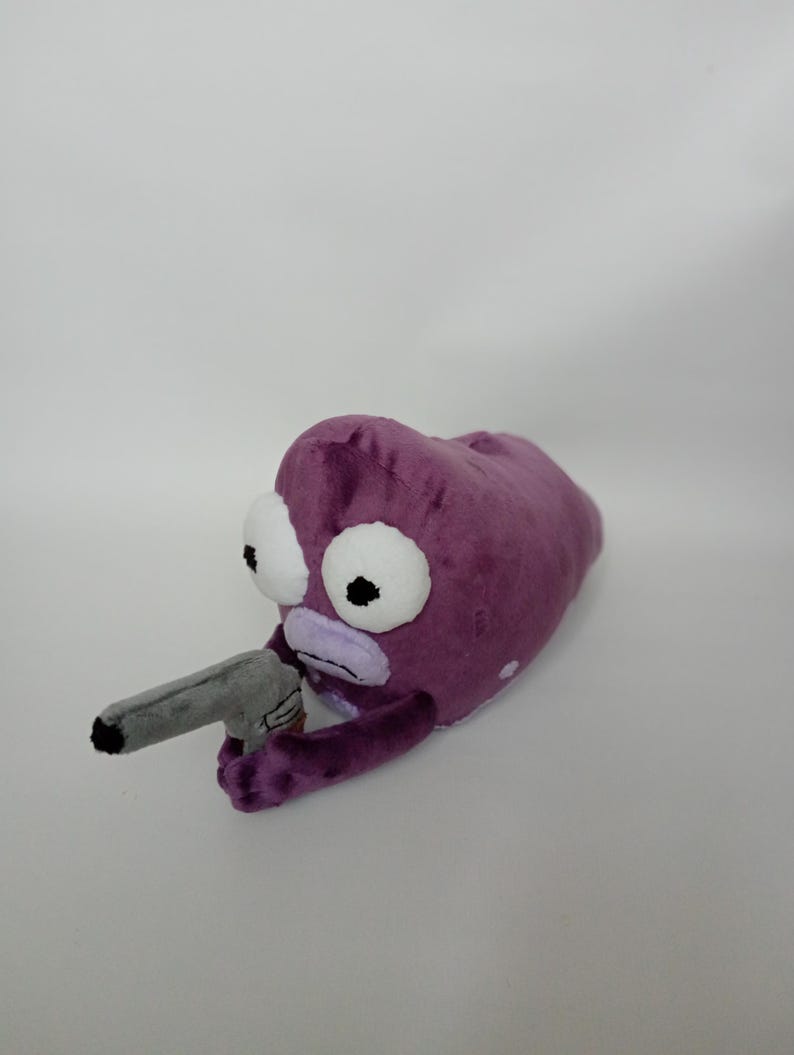 Puede incluir: Peluche con forma de alien&iacute;gena morado con grandes ojos blancos y una pistola de juguete gris. El peluche tiene una textura suave y aterciopelada y un dise&ntilde;o de dibujos animados, perfecto para los fans de la serie animada.
