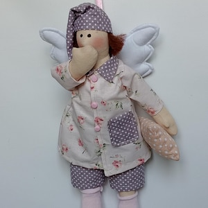 May include: A handmade doll dressed in pajamas with a floral print and polka dot accents. The doll has white wings, a nightcap, and is holding a small pillow. The doll is wearing pink socks and is suspended by a pink ribbon.