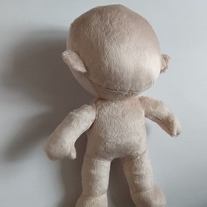 Op de afbeelding: Een beige pluche speelgoed met een rond hoofd, kleine oren en een eenvoudig lichaam. Het speelgoed staat op een wit oppervlak.