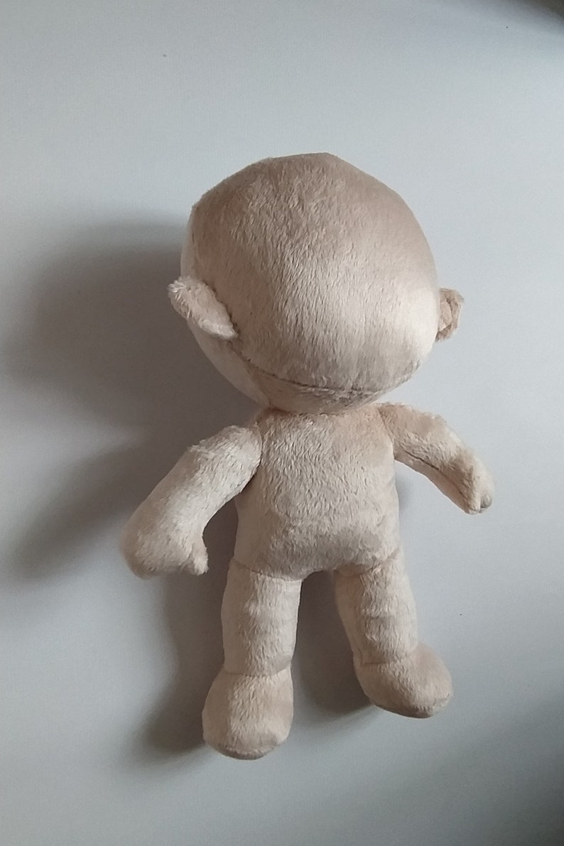 Op de afbeelding: Een beige pluche speelgoed met een rond hoofd, kleine oren en een eenvoudig lichaam. Het speelgoed staat op een wit oppervlak.