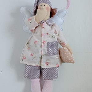May include: A handmade angel doll wearing pajamas and a nightcap. The doll's pajamas are white with a pink floral pattern, and the pants are gray with white polka dots. The doll has white wings and is holding a small pillow. The doll is approximately 8 inches tall.