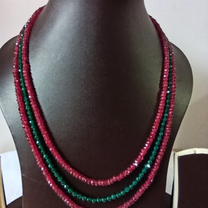 Könnte beinhalten: Eine dreireihige Halskette, die auf einer dunkelbraunen Schaufensterpuppe präsentiert wird. Die Halskette besteht aus abwechselnden Strängen aus roten und grünen facettierten Perlen. Die Perlen sind zu einem mehrschichtigen Effekt aufgereiht.