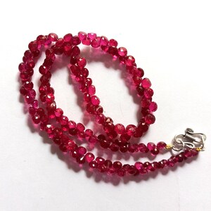 Peut inclure: Un collier composé de petites pierres précieuses rouge foncé à facettes. Les perles sont enfilées ensemble, formant plusieurs brins qui convergent vers un fermoir argenté. Les pierres précieuses ont un grand éclat, reflétant la lumière.