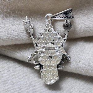 May include: A silver pendant with an intricate design. The pendant has a central honeycomb-like structure, with ornate arms extending outwards. The bail is a simple loop. The pendant is marked with "MR925".