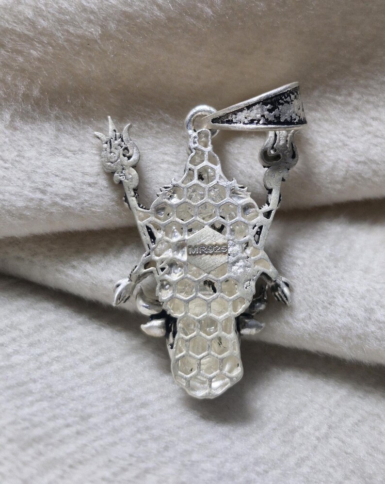 May include: A silver pendant with an intricate design. The pendant has a central honeycomb-like structure, with ornate arms extending outwards. The bail is a simple loop. The pendant is marked with "MR925".