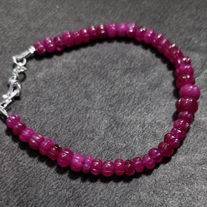 Op de afbeelding: Een armband van roze edelstenen met een zilveren sluiting. De armband is gemaakt van kleine, ronde kralen.