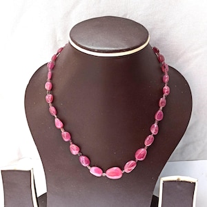 May include: A pink gemstone necklace displayed on a brown jewelry bust. The necklace features oval-shaped, polished pink stones strung together. The stones vary slightly in size and shade, creating a natural, organic look. The necklace is a beautiful piece of jewelry.