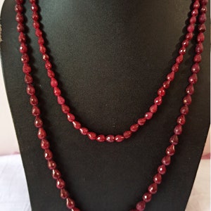Può includere: Una collana a doppio filo realizzata con perline di pietre preziose rosso scuro. Le perline sono sfaccettate e hanno una forma a goccia.