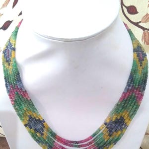 May include: A multi-strand necklace featuring a vibrant array of gemstones. The necklace showcases a pattern of green, yellow, blue, and pink beads. The necklace is displayed on a white bust against a patterned background.