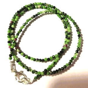 May include: A green, black and pink gemstone necklace with a silver clasp. The necklace is made of small, faceted beads.