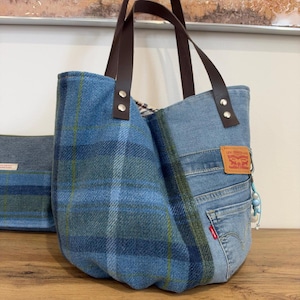 Pode incluir: Uma bolsa tote feita de tecido de lã xadrez azul e painéis de ganga azul claro. Possui alças de couro castanho escuro presas com rebites prateados, uma etiqueta de couro bege Levi Strauss & Co. e um pequeno pendente de contas azul.