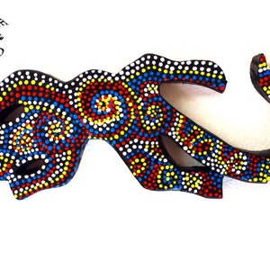 May include: A wooden wall hanging in the shape of a stylised lizard, painted with black, white, red and yellow dots. The lizard is curled up with its tail wrapped around its body.