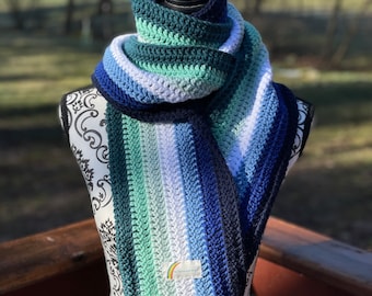 May include: A crocheted scarf with stripes of teal, light blue, white, and dark blue. The scarf is displayed on a mannequin with a white and black patterned torso.