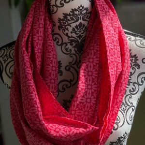 Puede incluir: Una bufanda infinita rosa con un estampado floral blanco. La bufanda está hecha de una tela suave y ligera, perfecta para añadir un toque de color a cualquier atuendo.