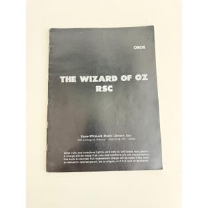 May include: A black music book for oboe titled The Wizard of Oz RSC. The cover features white text including the publisher Tams-Witmark Music Library, Inc. at 560 Lexington Avenue, New York, NY 10022, and instructions regarding pencil notations.