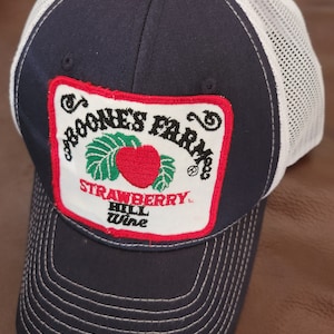 May include: A navy blue and white trucker hat with a red, white, and green patch that says "Boone's Farm Strawberry Hill Wine".