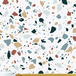 May include: A printable dollhouse wallpaper featuring a terrazzo pattern with white, beige, blue, green, and red chips. The wallpaper is shown in a miniature kitchen setting with a white pot on a wooden counter.