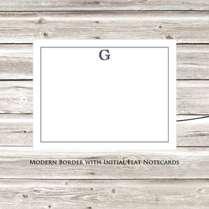May include: White flat notecards with a navy blue border and the letter "G" in the top center. The notecards are displayed against a woodgrain background. "MODERN BORDER WITH INITIAL FLAT NOTECARDS" is printed below the notecards.