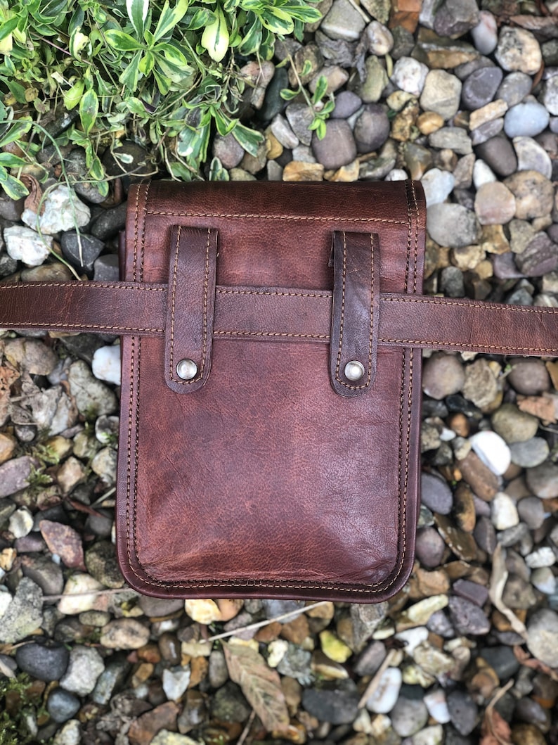 May include: A brown leather fanny pack with a belt loop and two adjustable straps. The bag has a flap with a buckle closure and a small pocket on the front.