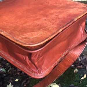 May include: A brown leather satchel bag with a long strap. The bag has a flap closure and is made of a distressed leather.