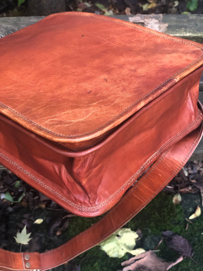 May include: A brown leather satchel bag with a long strap. The bag has a flap closure and is made of a distressed leather.