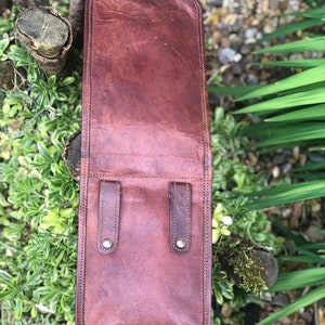 May include: A brown leather bag with two straps and silver buckles. The bag is closed and has a stitched edge.
