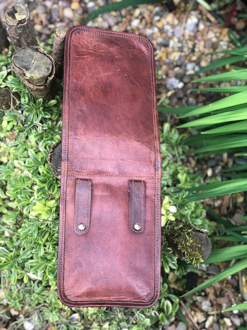 May include: A brown leather bag with two straps and silver buckles. The bag is closed and has a stitched edge.