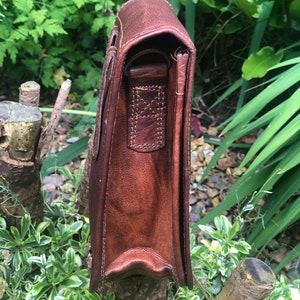 May include: A brown leather messenger bag with a flap closure and an adjustable shoulder strap. The bag has a worn, vintage look and is made of high-quality leather.