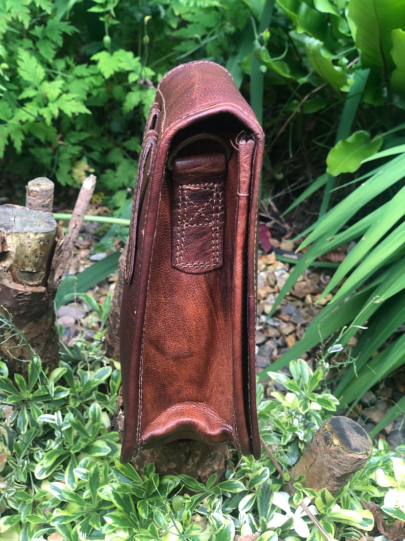 May include: A brown leather messenger bag with a flap closure and an adjustable shoulder strap. The bag has a worn, vintage look and is made of high-quality leather.