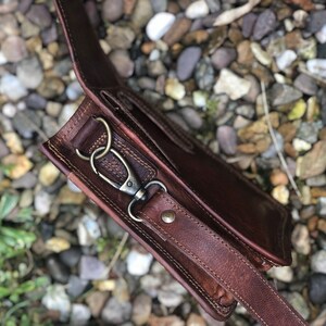 May include: A brown leather crossbody bag with a strap and a metal clasp. The bag is made of high-quality leather and has a vintage look.
