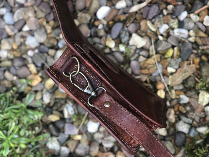 May include: A brown leather crossbody bag with a strap and a metal clasp. The bag is made of high-quality leather and has a vintage look.
