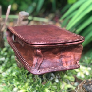 May include: A brown leather crossbody bag with a flap closure and a stitched design. The bag has a single strap and is made of a distressed leather.