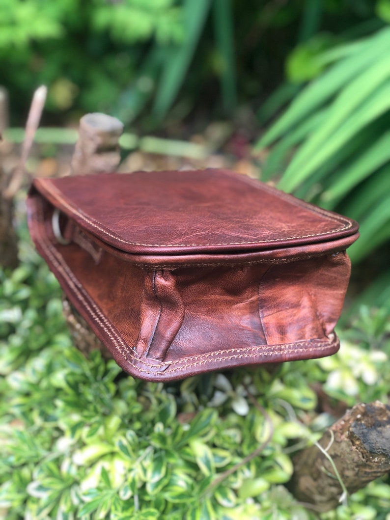 May include: A brown leather crossbody bag with a flap closure and a stitched design. The bag has a single strap and is made of a distressed leather.