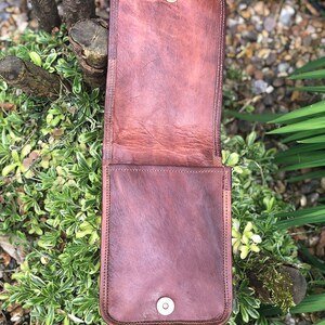May include: A brown leather phone case with a flap closure and two metal snaps. The case is open and the inside is visible.