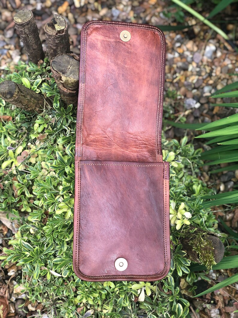 May include: A brown leather phone case with a flap closure and two metal snaps. The case is open and the inside is visible.