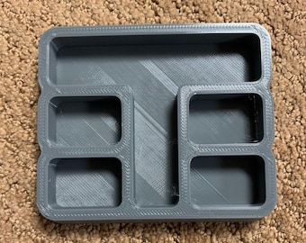 Può includere: Un organizzatore in plastica grigia con cinque scomparti. L'organizzatore ha una forma rettangolare ed è realizzato in un materiale testurizzato.