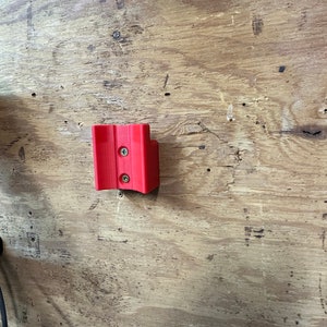 Op de afbeelding: Een rode plastic wandbevestiging met twee schroeven.