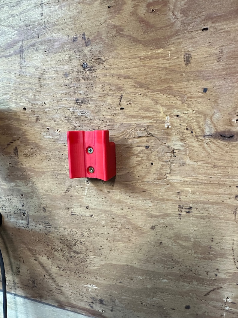 Op de afbeelding: Een rode plastic wandbevestiging met twee schroeven.