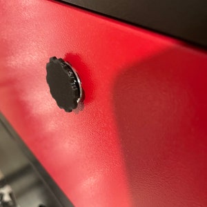 May include: A close-up of a red metal cabinet door with a black knob. The knob has a textured, circular design.