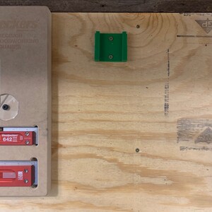 Op de afbeelding: Een groene kunststof jig voor houtbewerking, gemonteerd op een lichtbruin multiplex oppervlak.