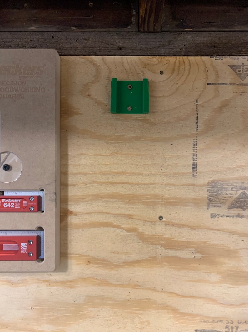 Op de afbeelding: Een groene kunststof jig voor houtbewerking, gemonteerd op een lichtbruin multiplex oppervlak.