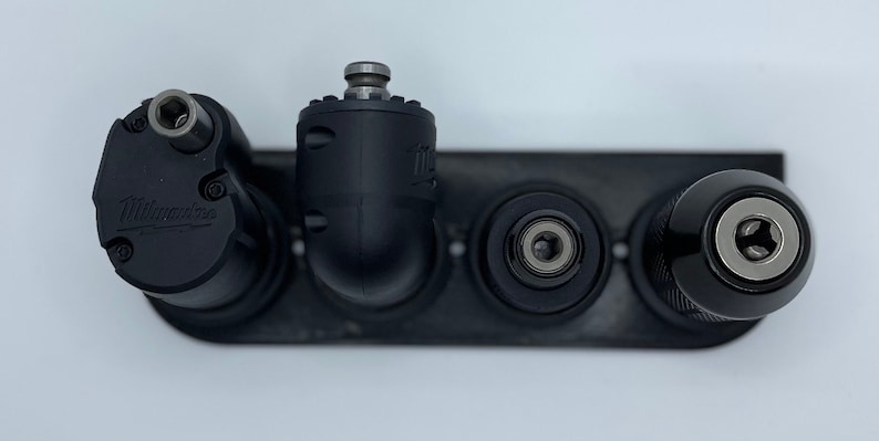 Puede incluir: Cuatro brocas de taladro negras con diferentes accesorios, incluyendo un accesorio de &aacute;ngulo recto, un accesorio recto y un accesorio de portabrocas. Las brocas de taladro est&aacute;n montadas en un bastidor de metal negro.