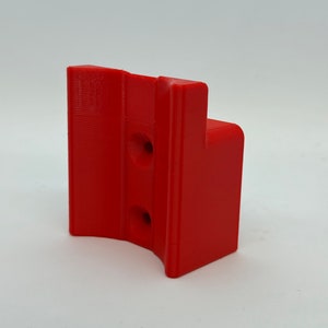 Op de afbeelding: Een rood plastic 3D-geprint onderdeel met twee gaten. Het onderdeel is gevormd als een beugel met een gebogen gedeelte.