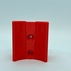 Op de afbeelding: Een rode 3D-geprinte beugel van plastic met twee gaten.