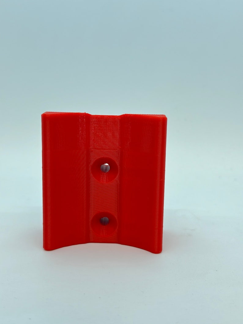 Op de afbeelding: Een rode 3D-geprinte beugel van plastic met twee gaten.