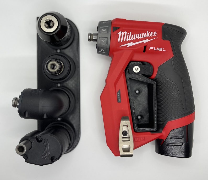 Puede incluir: Un taladro Milwaukee FUEL rojo y negro con un soporte para brocas negro y plateado. El taladro tiene un mango negro y un gatillo rojo. El soporte para brocas tiene tres brocas.