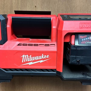 May include: A red Milwaukee M18 power tool charger with a black battery inserted. The charger has a digital display and a black handle. The battery is a Milwaukee REDLITHIUM battery.