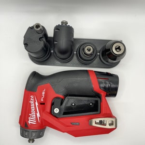 Puede incluir: Un taladro de &aacute;ngulo recto Milwaukee FUEL rojo y negro con un soporte de pl&aacute;stico negro que contiene cinco brocas diferentes. El taladro tiene un mango negro y un cuerpo rojo con la palabra "FUEL" impresa en &eacute;l. El taladro tiene un gatillo negro y un interruptor negro.