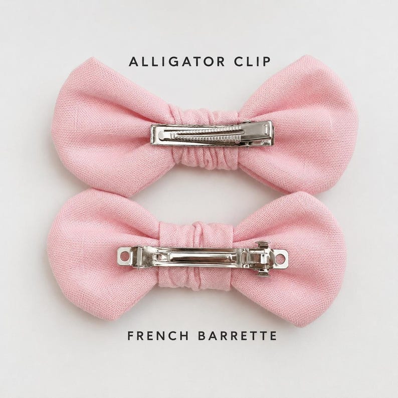 May include: Two light pink fabric bows. The top bow features a silver metal alligator clip, and the bottom bow features a silver metal French barrette. The text ALLIGATOR CLIP is above the top bow, and FRENCH BARRETTE is below the bottom bow.